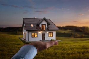 Man holding up a toy house in a field